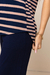 Detalhe de uma blusa feminina listrada em azul marinho e bege com uma mão segurando a parte inferior da peça.