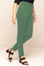 Calça bodycon verde, com cintura alta e detalhes em metal, vista de lado, combinada com sandálias de salto.