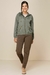 Mulher usando um corta vento com capuz verde, com calças marrons e sapatos claros, look confortável e moderno de inverno.