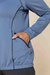 Detalhe de um conjunto térmico com jaqueta azul, mostrando o bolso com zíper e a manga com elástico.