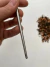Hashi de aço inox para bonsai posicionado sobre superfície branca ao lado de terra para plantio