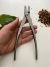 Alicate metálico para Jin e Shari sendo segurado por uma mão sobre superfície branca, com folha verde e terra ao fundo