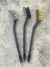 Kit de três escovas para limpeza de bonsai com cabos pretos e cerdas de metal, nylon e latão seguradas por uma mão.