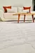 Tapete Roma Off White com textura, em um ambiente moderno, ao lado de um sofá claro e mesa de madeira.