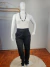 Calça plus size na cor preta, com cinto, combinada com uma blusa branca e colar, em ambiente neutro.