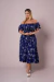 Mulher usando vestido plus size azul marinho estampado com flores brancas, modelo ombro a ombro com mangas bufantes e comprimento midi