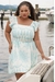 Modelo usando um vestido plus size balonê azul claro com estampa floral à beira de um lago.