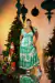 Modelo vestindo um vestido plus size estampado em off white e verde, posando em frente a uma árvore de Natal decorada.