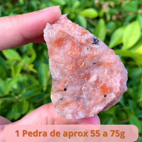 Pedra do Sol verdadeira, cristal natural em forma bruta, pesando entre 55 a 75g, sendo segurada por uma mão.