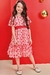 Menina usando um vestido em chiffon com estampa de corações em tons de rosa e vermelho, posando em frente a um fundo vermelho.