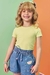 Menina sorrindo usando uma blusa canelada verde e shorts jeans com detalhes coloridos.