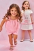 Duas meninas sorrindo, uma vestindo blusa rosa e shorts, e a outra em vestido branco com estampa de gatinhos.