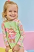 Criança sorridente usando um conjunto de blusa e calcinha em malha com estampa divertida e proteção UV, em cenário colorido.