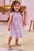 Menina sorridente usando um vestido lilás de nylon e tule com estampas de borboletas, em um ambiente decorado com móveis clássicos.