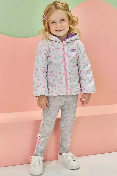 Criança sorridente usando um conjunto infantil de jaqueta dupla face com estampa de bolinhas e calça legging cinza com detalhes de estampa.