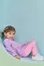 Menina sorridente usando um conjunto de bata em malha de textura quadradinhos e calça legging rosa.