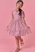 Menina sorrindo usando um vestido infantil em tule rosa com detalhes em coração, posando em um fundo rosa.