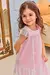 Menina sorrindo usando um vestido infantil rosa com detalhes em tule e flores, em um ambiente aconchegante.