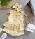 Conjunto amarelo para menina de 6 anos, composto por blusa com laços e shorts, acompanhado de um laço de cabelo e uma bolsa branca.