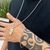 Cordão baiano banhado a prata de 2mm com pingente, usado por uma pessoa com tatuagem no braço e pulseira de prata.