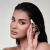 Mulher com pele maquiada segurando frasco pequeno transparente com conta-gotas do produto Seal Pro Blindagem Incolor Lara Beauty