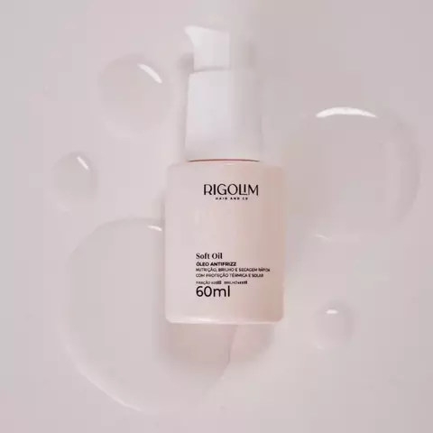 Frasco branco fosco de 60ml do óleo antifrizz Soft Oil da Rigolim Hair & Co com pump, sobre superfície com gotas de óleo transparente