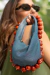 Mulher segurando uma bolsa azul com detalhes em pérolas e contas vermelhas, usando óculos escuros.