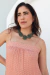 Modelo usando um colar estruturado com pedras turquesas, destacando-se sobre uma blusa de alças finas com padrão em tons de rosa e branco.