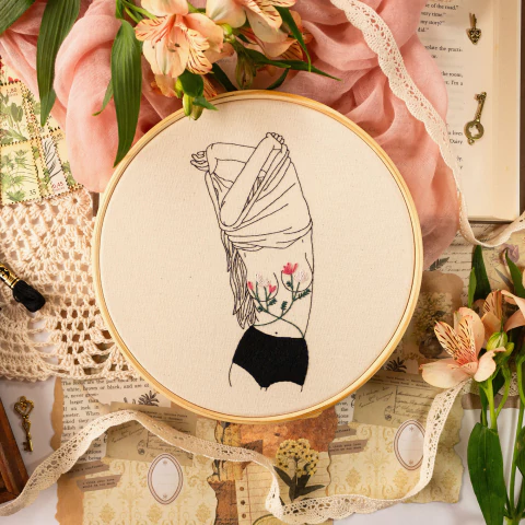 Quadro bordado a mão de mulher tirando blusa com flores nos seios.