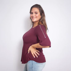 Modelo mujer sonriente de perfil usando remera Piove color vino con mangas tres cuartos y detalles reflectantes en frente y mangas