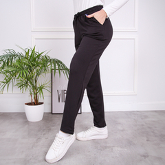 Pantalones babucha Angela en color negro, con un diseño cómodo y moderno, mostrados junto a una planta decorativa.