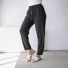 Pantalones negros tipo babucha Guada, con cintura elástica y ajuste, combinados con sandalias blancas.