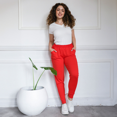 Modelo posando con babuchas rojas y camiseta blanca, junto a una planta en maceta blanca.