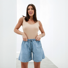 Modelo luciendo un conjunto de bermudas de denim claro con una camiseta de tirantes beige.