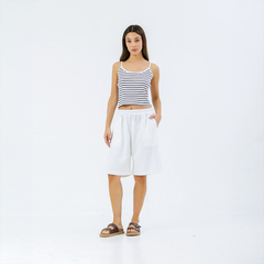 Modelo vistiendo bermudas blancas y top de rayas, posando en un fondo blanco.