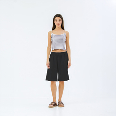 Mujer de pie luciendo bermudas negras y top de rayas en un fondo blanco.