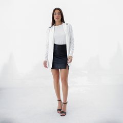 Modelo usando un blazer blanco con una blusa blanca y una falda de cuero negra, posando en un fondo blanco.