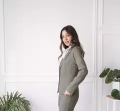 Modelo luciendo un blazer Hada de color verde, con fondo blanco y plantas decorativas.