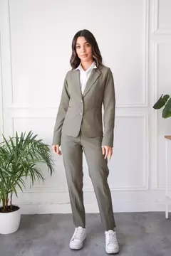 Modelo luciendo un blazer Hada de color verde, combinado con camisa blanca y zapatillas deportivas, en un ambiente luminoso con plantas.