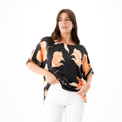 Modelo luciendo una blusa Acalia con estampado de hojas en tonos naranja sobre fondo negro.