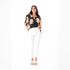 Modelo luciendo una blusa negra con estampado de hojas en tonos naranjas, combinada con pantalones blancos y sandalias.