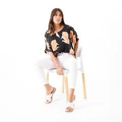 Modelo sentada con blusa Acalia de estampado floral negro y pantalones blancos.