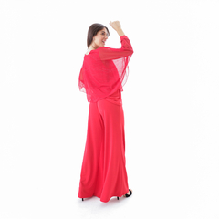 Pantalón palazzo rojo de mujer con blusa transparente, visto desde atrás.
