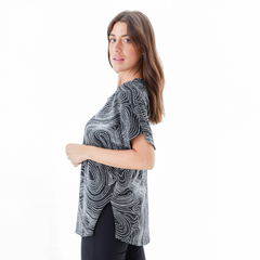 Modelo usando una blusa negra con un diseño de líneas en blanco, vista lateral.