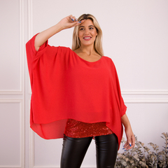 Blusa Alas en color rojo, con un diseño amplio y elegante, combinada con una camiseta brillante debajo y pantalones ajustados.