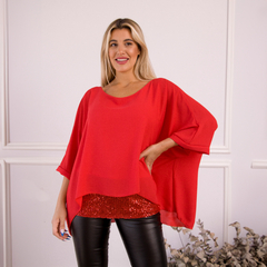 Blusa roja de estilo elegante con mangas amplias, combinada con una falda brillante, modelada por una mujer sonriente en un entorno decorativo.