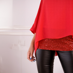 Blusa roja con mangas amplias y detalles brillantes en la parte inferior, combinada con pantalones negros ajustados.