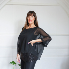 Blusa negras con mangas amplias, combinada con una prenda brillante, presentada por una modelo en un ambiente elegante.