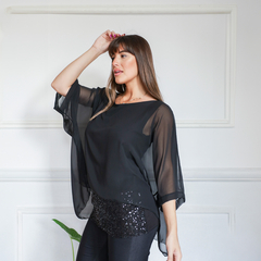 Blusa negra con mangas amplias y detalles de lentejuelas en la parte inferior, modelada por una mujer en un ambiente elegante.