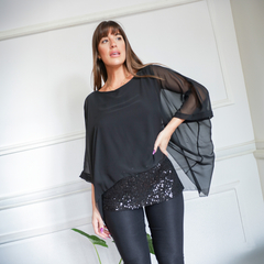 Blusa Alas de color negro con mangas amplias y detalles de lentejuelas en la parte inferior, combinada con pantalones oscuros.